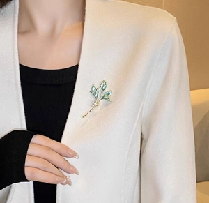 Détail de la broche fleur de lys avec dégradé vert et perles sur un manteau blanc