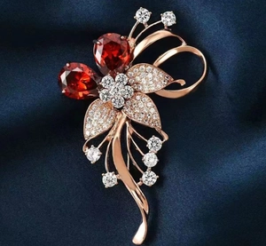 Détail d'une broche florale en or rose avec gemmes rouges et strass blancs brillants