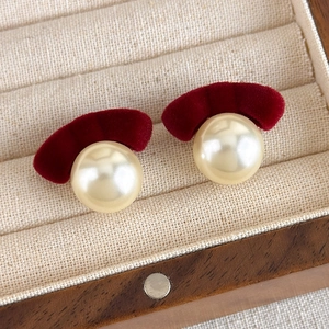 Detailed close-up of red velvet bow and large cream pearl earrings in a wooden jewelry box