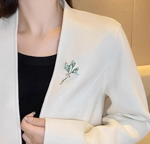 Broche fleur de lys élégante en émail vert et zircons sur le revers d'un manteau blanc