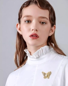 Close-up of golden butterfly brooch with rhinestones and pearl on white blouse