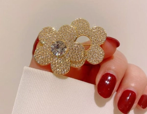 Close-up of golden floral brooch with micro-pave crystals and a central diamond on fabric