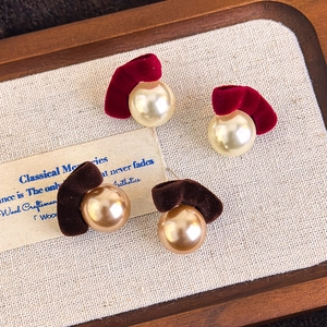 Macro view of velvet bow earrings with large pearls on a wooden tray with a vintage vibe