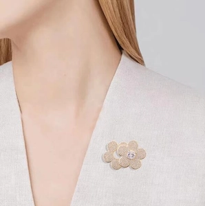Elegant gold double flower brooch with white cubic zirconia crystals on cream coat