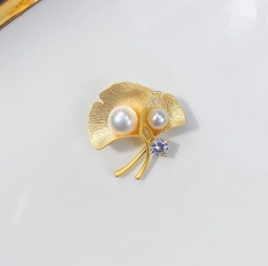 Macro detail of golden ginkgo leaf brooch with brushed texture and white pearls