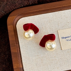 Macro detail of dark red velvet bow earrings with large round cream pearls on a wooden tray