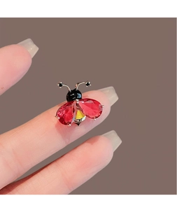 Vue macro détaillée d'une broche coccinelle en cristaux rouges posée sur le bout du doigt