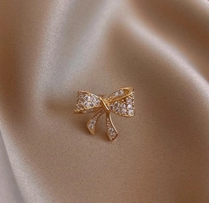 Dettaglio della raffinata spilla a fiocco dorato con zirconi su raso color champagne