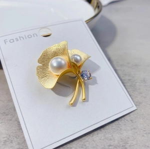 Detail of matte gold ginkgo leaf brooch featuring white pearls and a blue zircon stone
