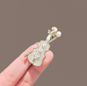 Detailed view of a gold violin brooch featuring sparkling rhinestones and a white pearl