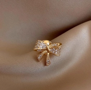 Elegante spilla a fiocco dorata con strass pavé su lussuoso sfondo di raso champagne
