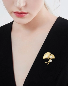 Detailed close-up of golden ginkgo leaf brooch with white pearls and zircons on black fabric