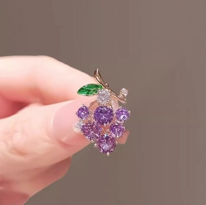 Macro detail of purple grape brooch featuring cubic zirconia and green enamel leaf