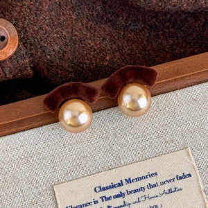 Detail of vintage champagne pearl earrings with dark brown velvet bow on wooden frame