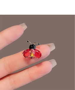 Détail d'une petite broche coccinelle avec des ailes en cristal rouge et métal doré