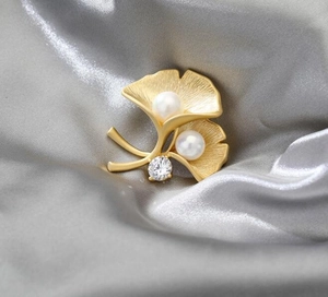 Macro shot of gold ginkgo leaf brooch with matte texture and white pearls