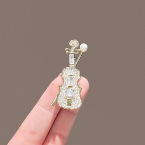 Close-up of violin brooch with sparkling zircons and pearl held by fingers