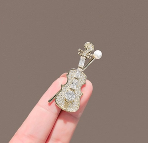 Detailed close-up of a golden violin brooch with sparkling zircons and a white pearl accent