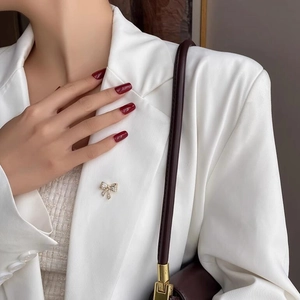Elegante spilla a fiocco dorata con zirconi bianchi fissata sul bavero di un blazer bianco