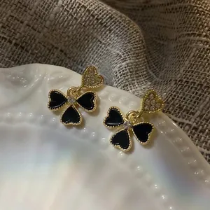 Close-up of golden heart studs with black clover pendants and sparkling crystals