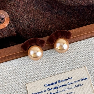 Macro detail of vintage brown flocked bow earrings with polished pearl studs on knit fabric
