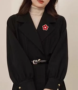 Detail view of a vintage floral brooch with red petals and rhinestones on a black coat lapel