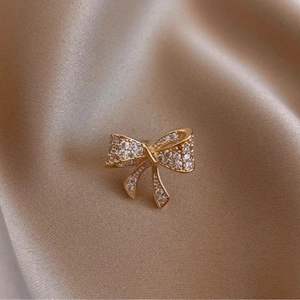 Elegante spilla a fiocco dorata con scintillanti cristalli micro-pave su sfondo di seta