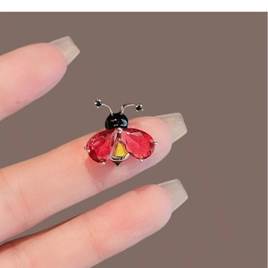 Délicate broche coccinelle en cristal rouge et plaqué or tenue entre les doigts