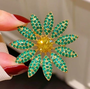 Luxury maple flower brooch with green crystals and yellow center stone held in hand