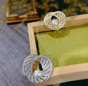 Macro detail of gold and silver circular swirl brooches with pearls and micro-set crystals