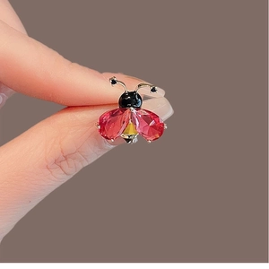 Élégante broche coccinelle en cristal rouge avec dorure tenue entre les doigts