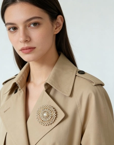 Close-up of a golden sunburst brooch with a large pearl on a classic camel coat lapel