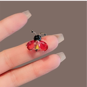 Broche insecte dorée avec cristaux gouttes rouges et centre jaune tenue en main