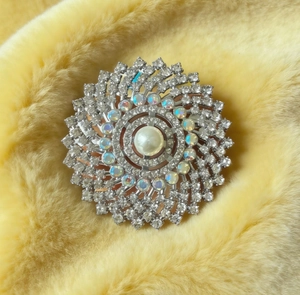 Detailed close-up of a silver-toned sunburst brooch featuring pearls and iridescent crystals