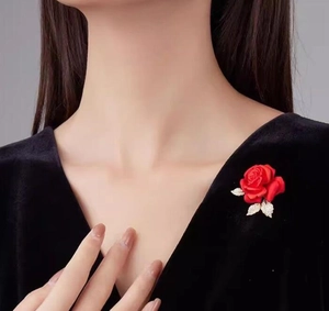 Détail d'une broche rose en velours rouge avec feuilles dorées sur tissu noir