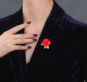 Détail d'une broche rose rouge avec feuilles dorées sur un revers en velours bleu
