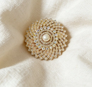 Close-up of golden sunflower brooch featuring a large pearl and sparkling rhinestones