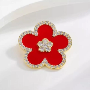 Macro shot of elegant five-petal flower brooch with red filling and diamond-set gold edges