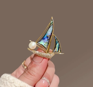 Détail de la broche voilier doré avec nacre d'abalone et perle blanche élégante