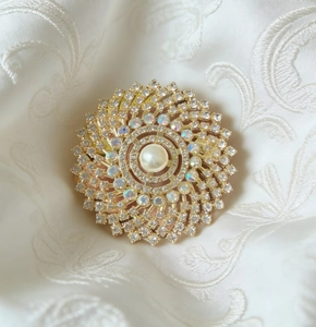 Detailed view of luxury golden brooch featuring central pearl and radiant crystal accents