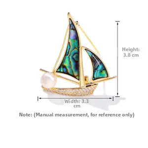 Vue détaillée d'une broche voilier dorée avec voiles en nacre et une perle blanche