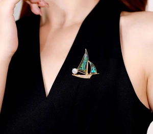 Détail d'une broche voilier de luxe dorée avec perles et incrustations en nacre colorée