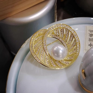 Detailed close-up of a vintage pearl brooch with gold hollow spiral rings and zircons