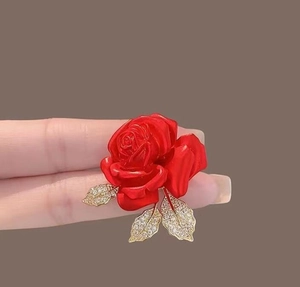 Détail macro d'une broche rose rouge avec des feuilles dorées et des cristaux