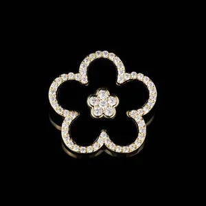 Elegant gold-trimmed black five-petal flower brooch with pavé set crystals on a black surface