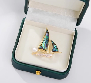 Détail macro de la broche voilier avec nacre d'abalone, perles et zircons en boîte à bijoux