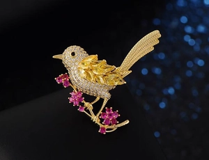 Dettaglio macro di spilla a uccello con pietre gialle e fiori rosa su sfondo blu