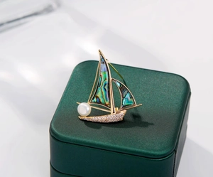 Gros plan détaillé d'une broche voilier dorée avec nacre d'abalone et perle blanche