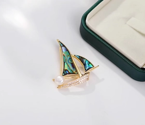 Détail de la broche voilier dorée avec incrustation d'abalone irisée et perle élégante