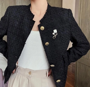 Detailed close-up of white magnolia brooch with pearl on a black tweed blazer jacket